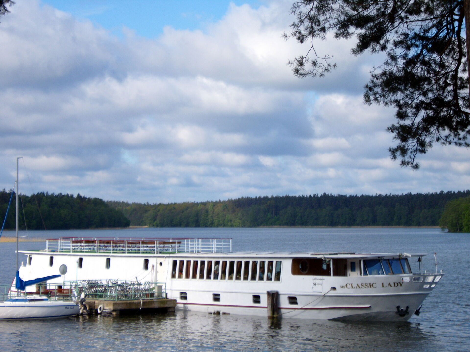 Mit Rad und Schiff durch Masuren Ein Schiff fährt auf einem See in den Masuren und im Hintergrund ist ein Wald
