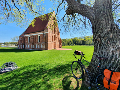 Radtour von Vilnius zur Kurischen Nehrung Ein Fahrrad steht an einem Baum und links daneben befindet sich eine rote Kirche