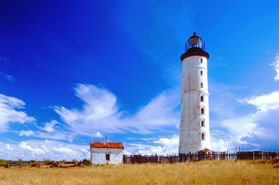7-tägige Radtour auf den estnischen Inseln Ein weißer Leuchtturm und links daneben befindet sich ein kleines, weißes Haus vor Gräsern