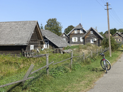Radtour entlang der litauischen Seen Ein Fahrrad steht an einem Zaun vor mehreren Holzhütten in der Natur