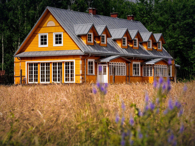 Ferienhaus - Nature Lodge im Bialowieza-Urwald Ein gelbes, großes und modernes Holzhaus auf einem Feld und im Hintergrund ist ein Wald