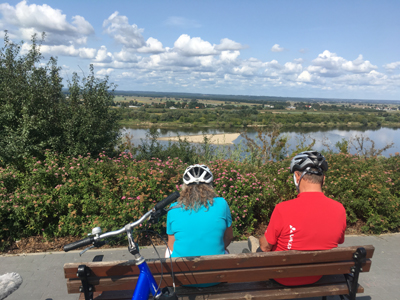 Radtour Warschau - Danzig Ein Mann und eine Frau sitzen mit Ihren Fahrradhelmen auf einer Bank und schauen auf einen Fluss