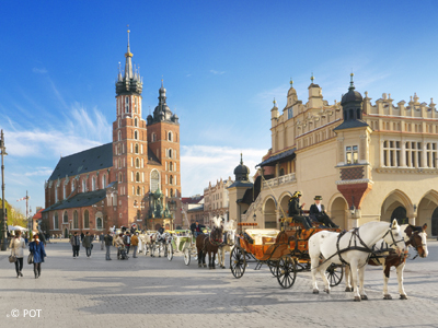 Radtour von Krakau nach Warschau Mehrere Pferdekutschen stehen vor zwei großen Gebäuden und links daneben laufen Menschen lang