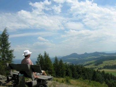 Wanderreise durch die Beskiden Ein Mann mit einem weißen Hut sitzt auf einer Bank und schaut auf die Berge und die Wälder