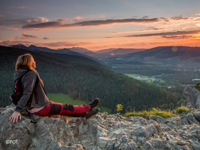 Wander-Wochenende Tatra Eine Frau in Wanderkleidung sitzt auf einem Stein und schaut sich den Sonnenuntergang auf einem Berg an