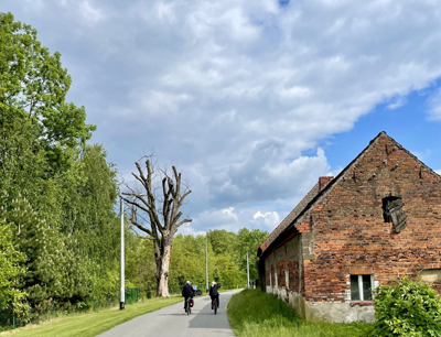 Radtour Breslau und Niederschlesien Zwei Personen fahren auf einem Fahrradweg. rechts befindet sich ein altes Haus und links befinden sich Bäume