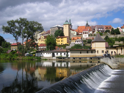 Bäderradtour von Franzensbad nach Prag Im Vordergrund ist ein Wasserfall und im Hintergrund ist eine Stadt mit mehreren Wohnungen und einer Kirche