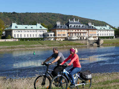 Individuelle Radtour von Prag nach Dresden Zwei Personen fahren mit dem Fahrrad an der Elbe entlang und im Hintergrund sind Häuser