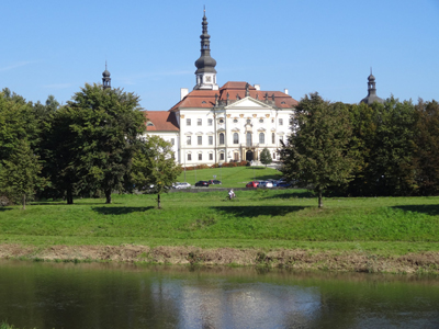 Radtour durch Mähren Im Vordergrund ist ein See und dahinter befindet sich ein Gebäude mit Bäumen und Autos davor