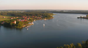 Eine Luftaufnahme eines Sees  mit Segelbooten drauf und links daneben ist ein kleines Dorf in Polen zu sehen