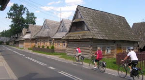 Eine Straße mit drei Radfahrern führt durch eine altes Dorf in Polen