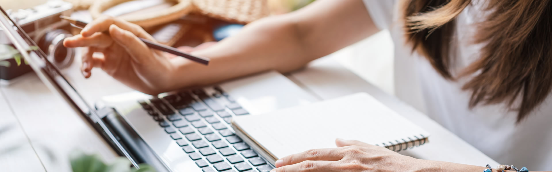 Eine Frau sitzt am Computer und bucht eine Polenreise. Auf dem Computer liegt ein Notizblock