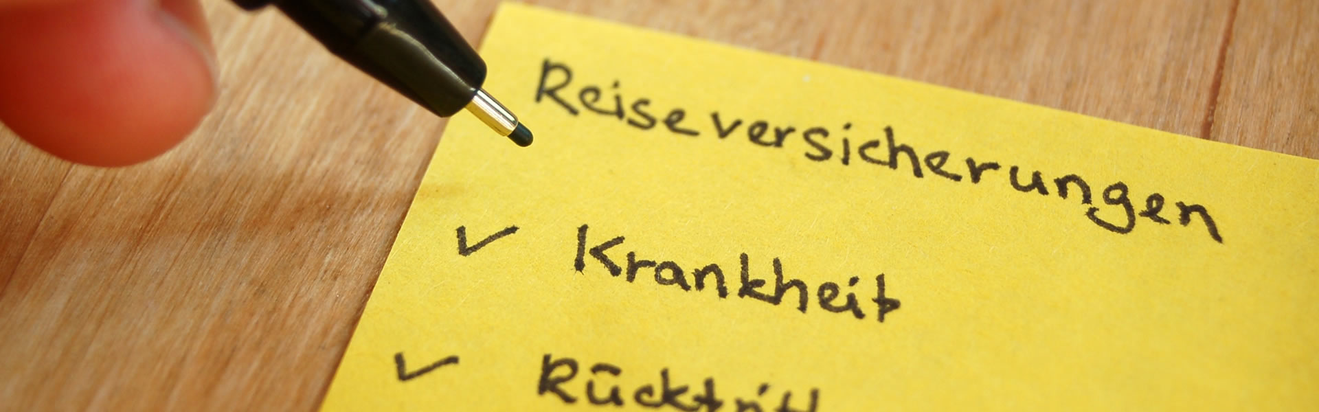 Eine Person schreibt auf einen gelben Notizzettel Reiseversicherungen, Krankheit, Rücktritt...
