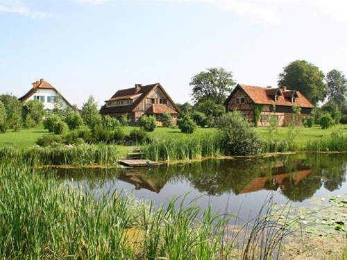 Drei moderne Häuser stehen zwischen Grässern, Bäumen und Büschen und davor befindet sich ein See in Polen